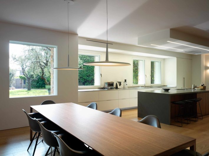 View of the open plan kitchen and dining area with built-in fixed and flush-to-the-wall white lacquered windows